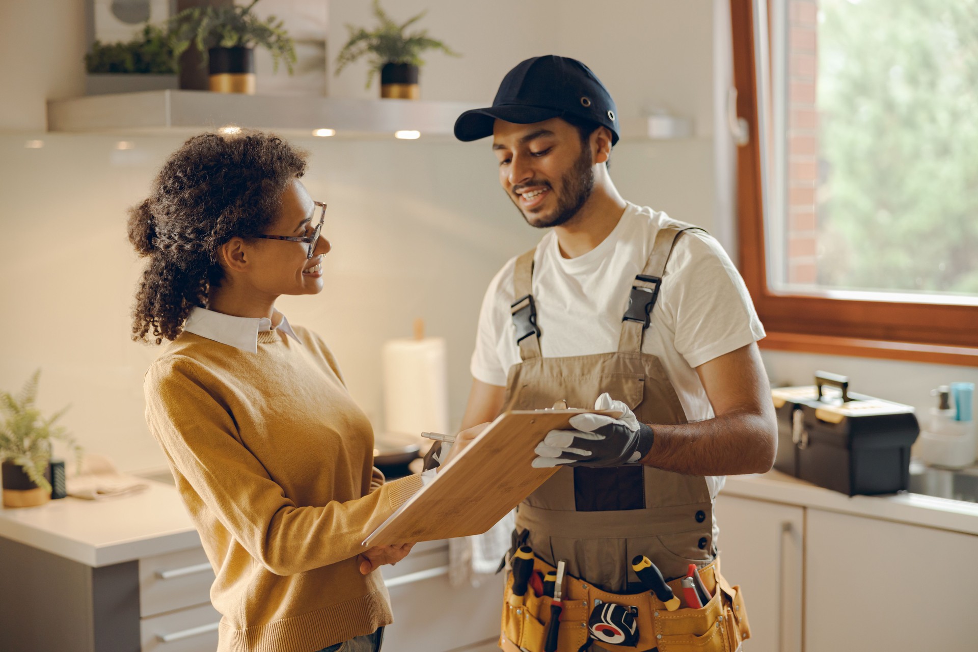 Smilng young woman signing document while communicating with handyman at the kitchen